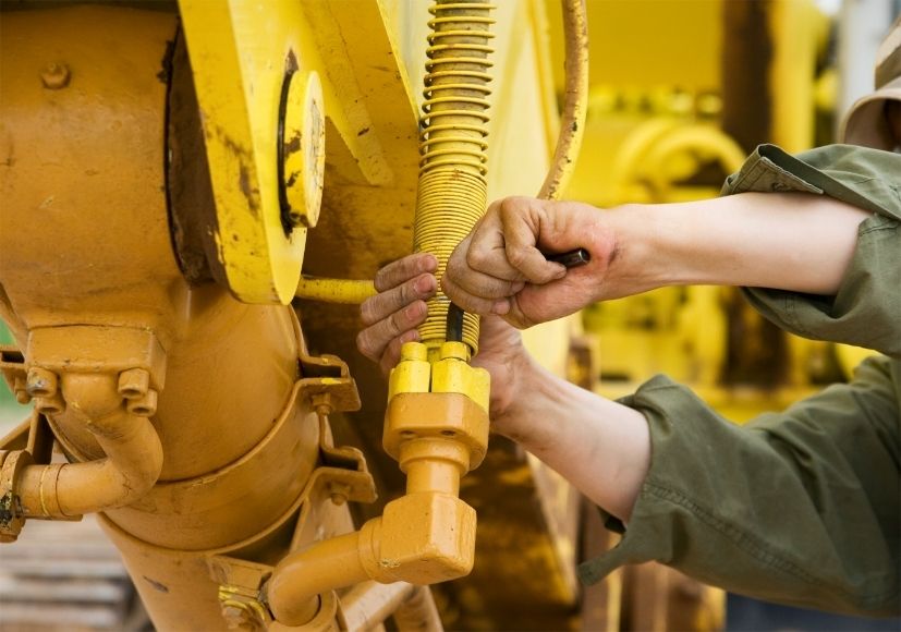 Wartungsarbeiten an der Hydraulik einer gelben Baumaschine